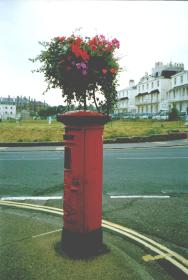 Red pillar box with flower basket on top.